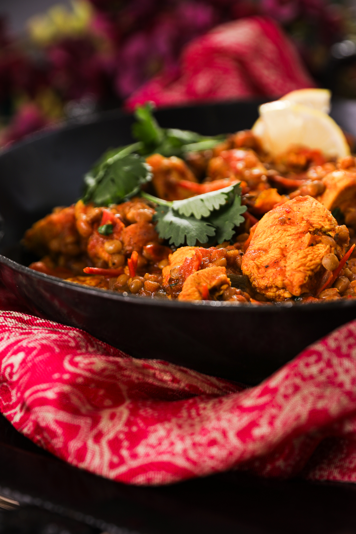 Perspective view of chicken and lentils, garnished with fresh cilantro, lemon slices styled with a pink dupatta scarf.