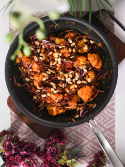 Pan filled with stir-fried cabbage and cauliflower, generously topped with peanuts styled around flowers.