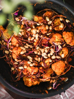 Close-up image of pan of stir fired cabbage and cauliflower topped with peanuts.