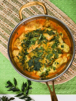 Top view of pan of fish fillets submerged in a vibrant curry sauce topped with chopped cilantro.