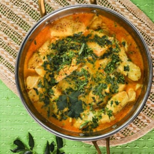 Top view of pan of fish fillets submerged in a vibrant curry sauce topped with chopped cilantro.