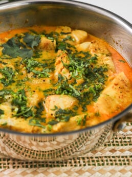 Half-view: Pan of cod fish fillets bathing in curry sauce, garnished with chopped cilantro.