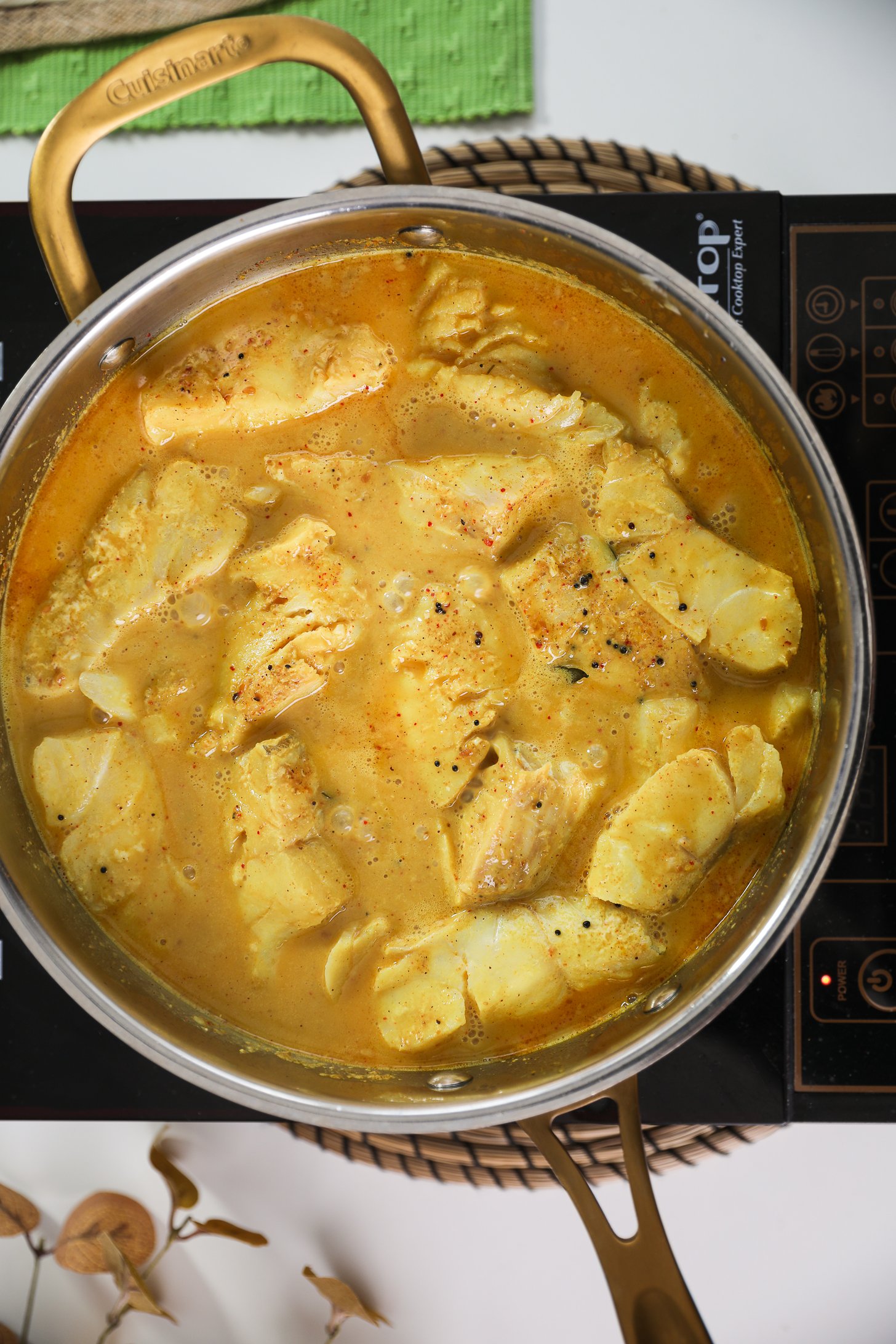 Pan of fish fillets simmering in a curry sauce on a mobile cooktop.