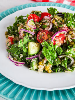 Angled top view image showcasing a vibrant salad comprising kale, quinoa, cucumber, tomatoes, and mung beans sprinkled with a redish powdered spice.