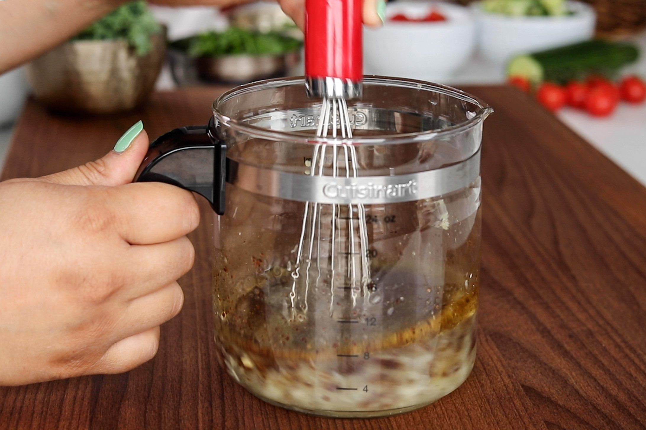 A hand holding a whisk and a jar mixing salad dressing ingredients.