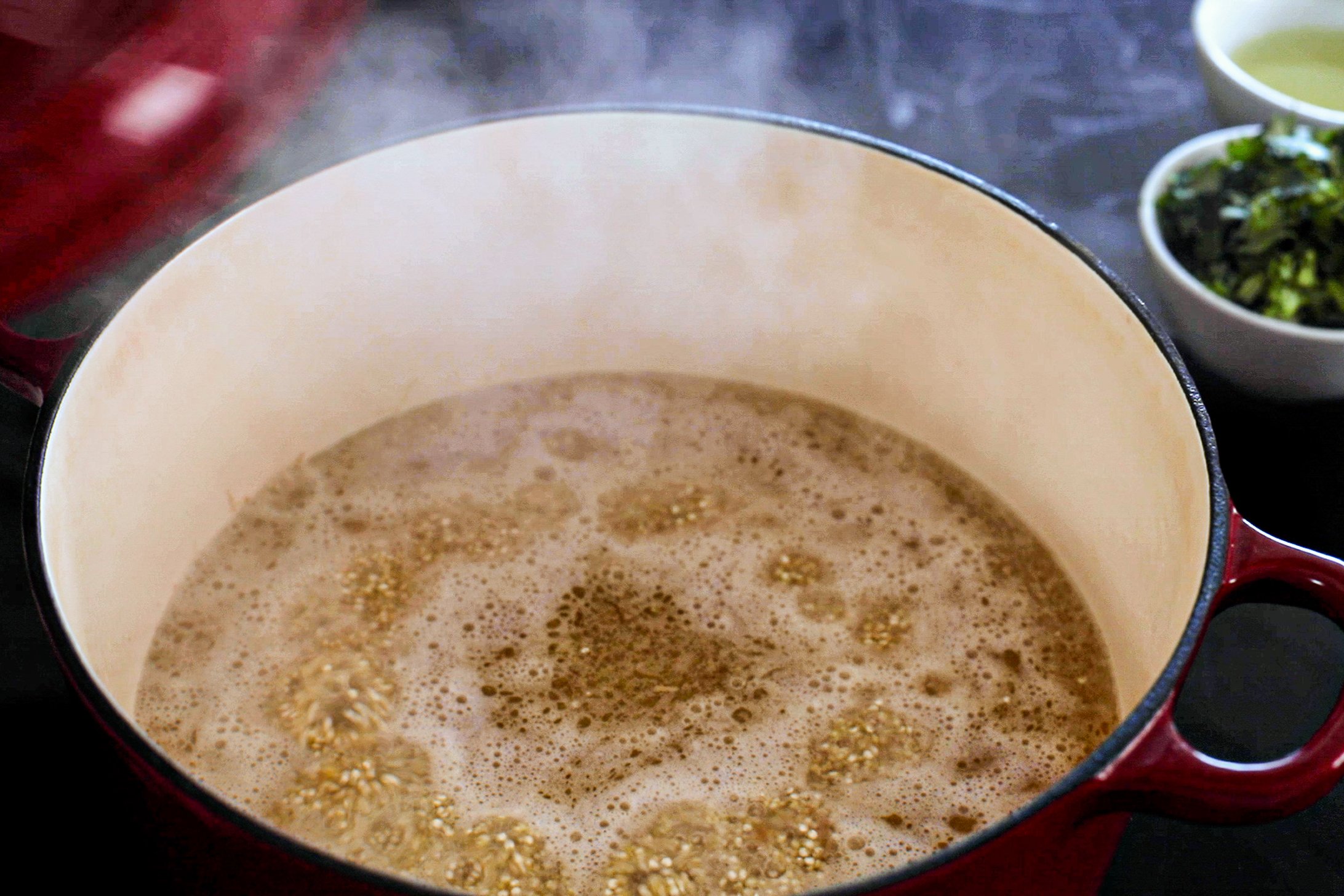 A cast iron pot with quinoa boiling in water with steam being produced.
