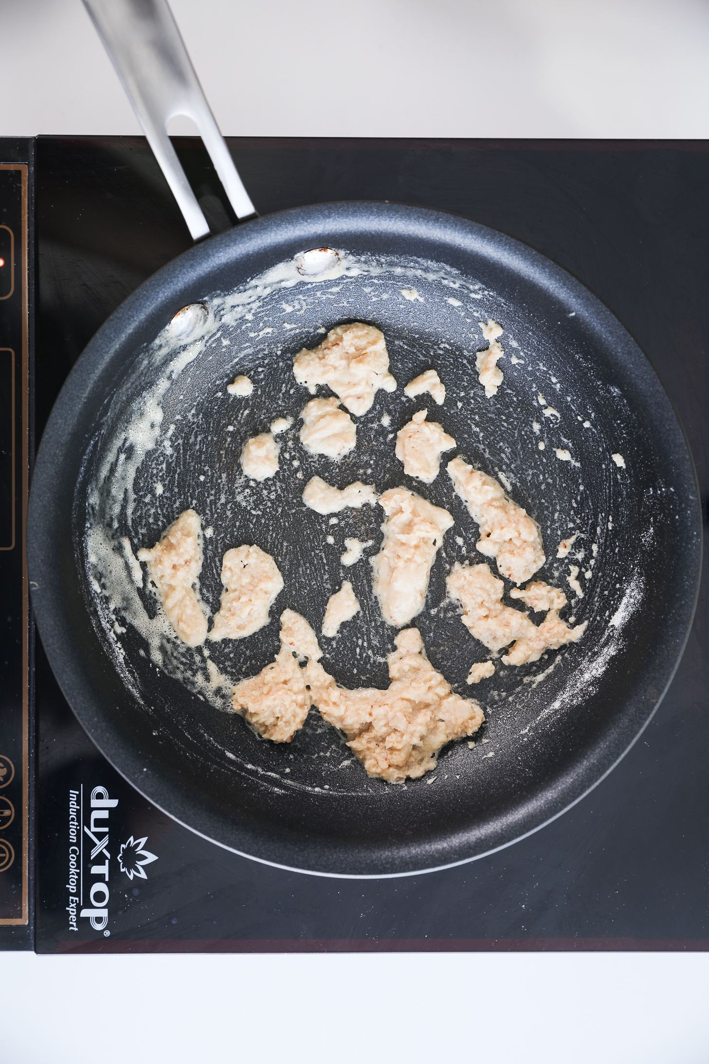 A pan with flour and butter lumps (making roux) placed on a mobile cooktop.