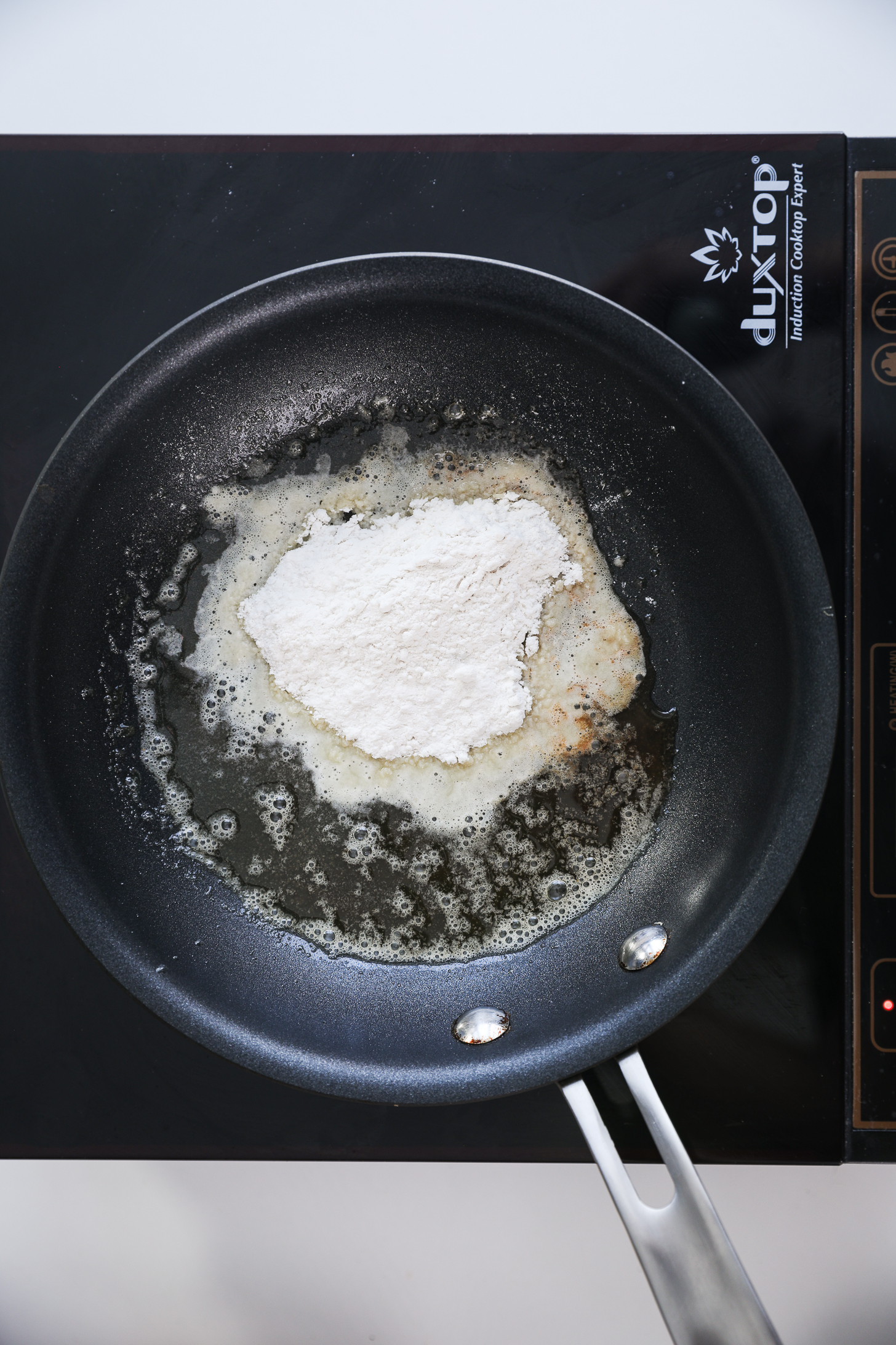 A pan with flour and melted butter (making roux) placed on a mobile cooktop.