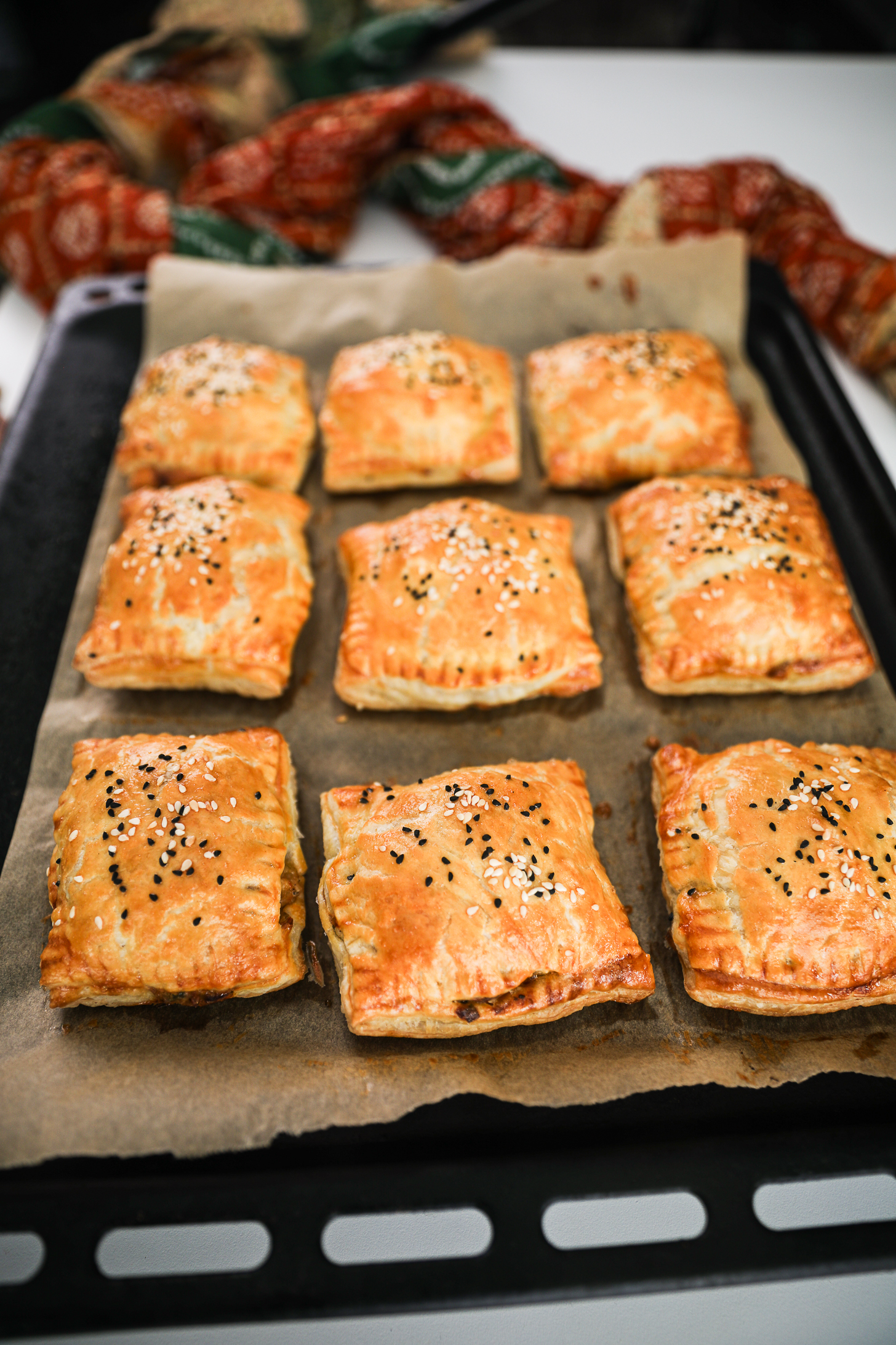 A lined oven tray of baked golden puff pastries topped with seeds.