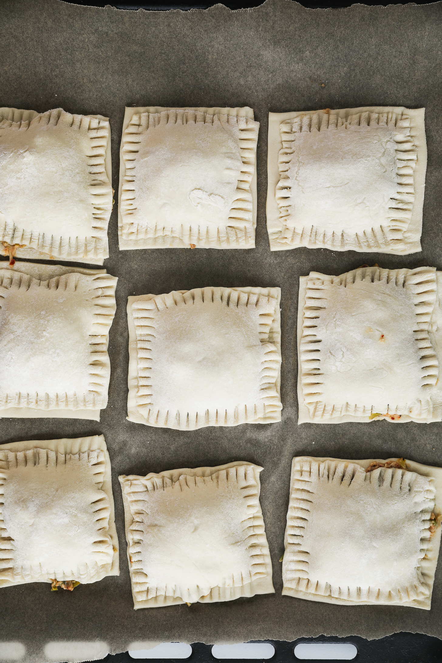 Top-down image of an oven tray lined with unbaked puff pastry squares, each filled with a filling.