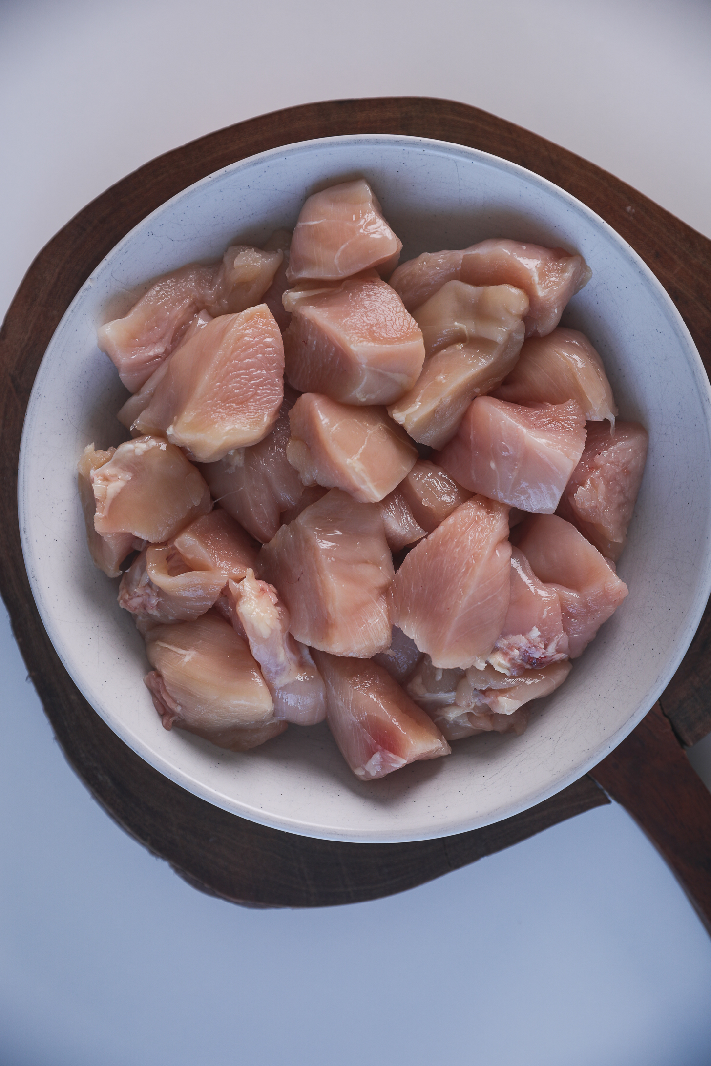 A bowl of chicken breast pieces placed on a wooden board against a white background.
