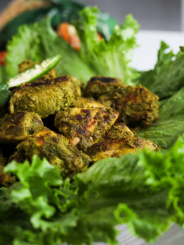 Perspective image of green chicken (Hariyali chicken) breast pieces placed on lettuce leaves.