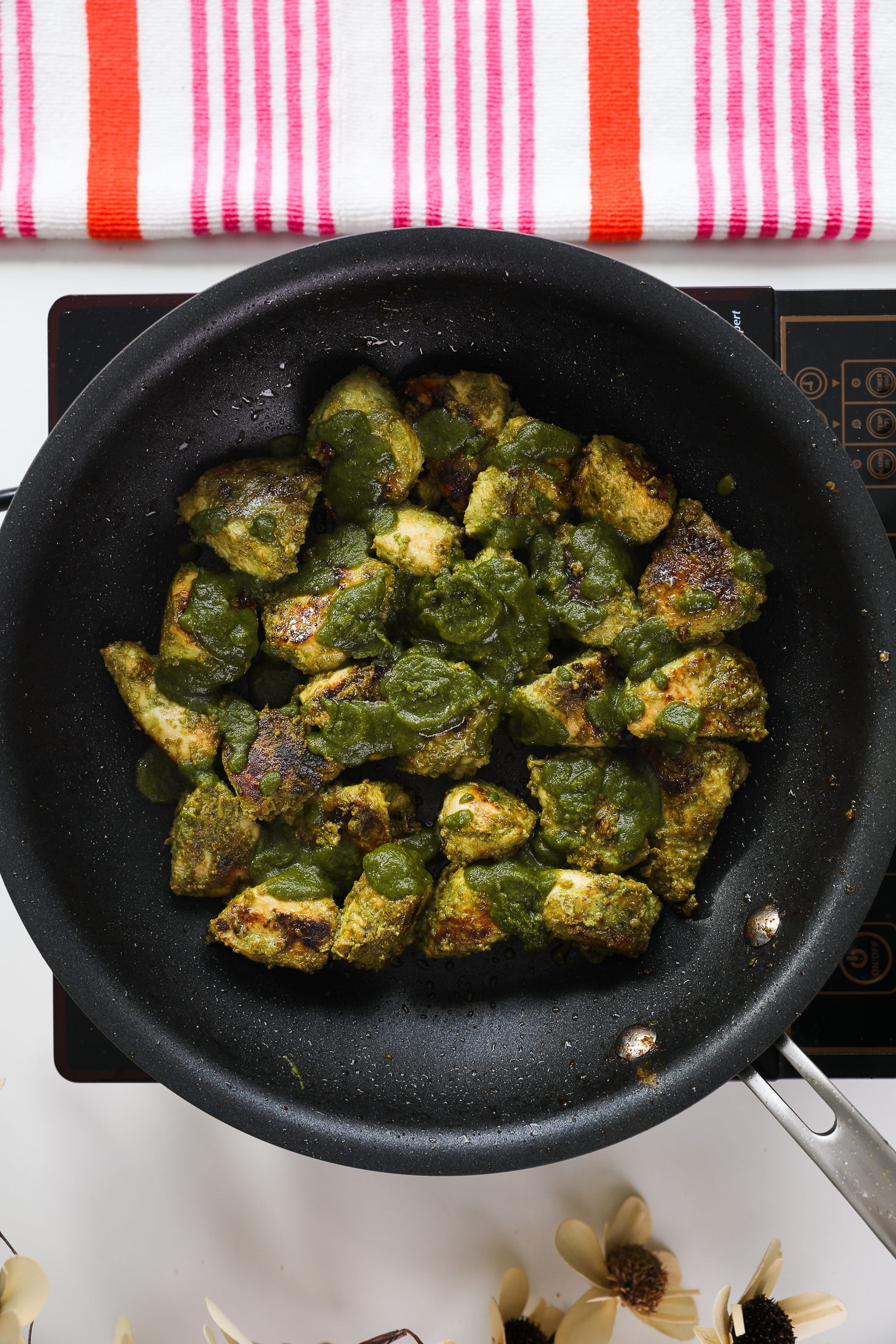 Pan of cooked and charred green masala-coated chicken breast pieces topped with green hara masala sauce.