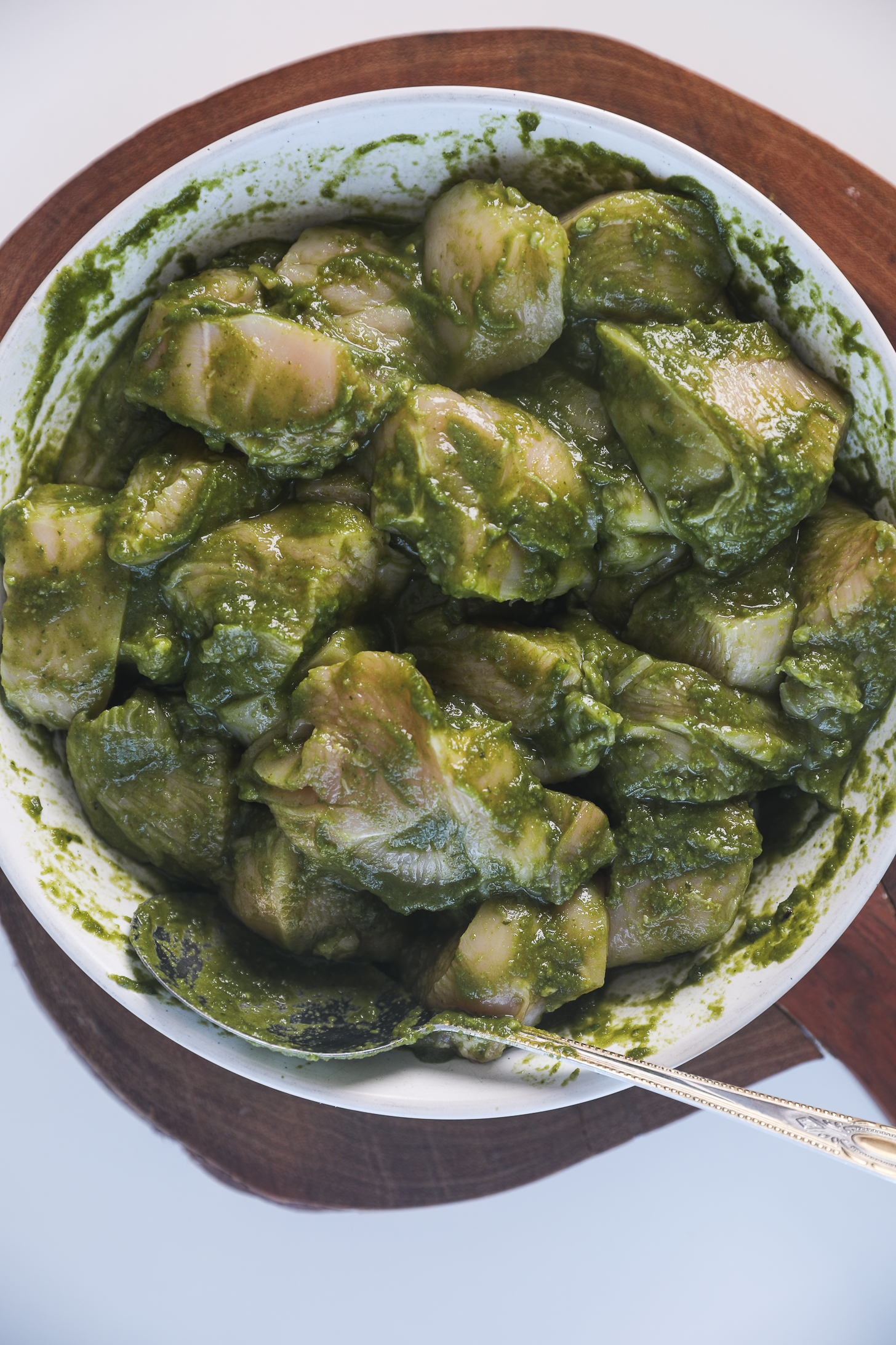 Chicken pieces coated in a green chutney (sauce) in a bowl with a large spoon alongside.