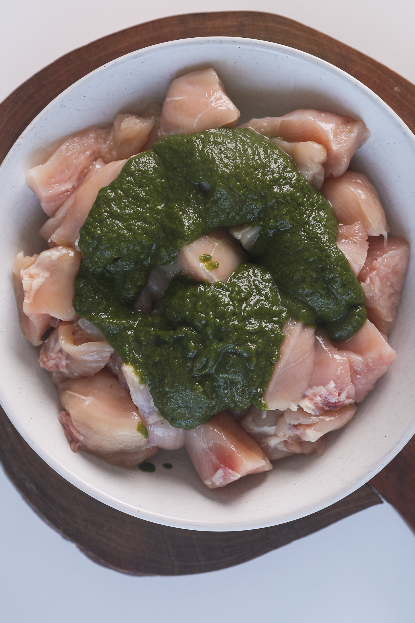 A green cilantro chutney (sauce) poured over a pile of chicken breast pieces in a bowl.
