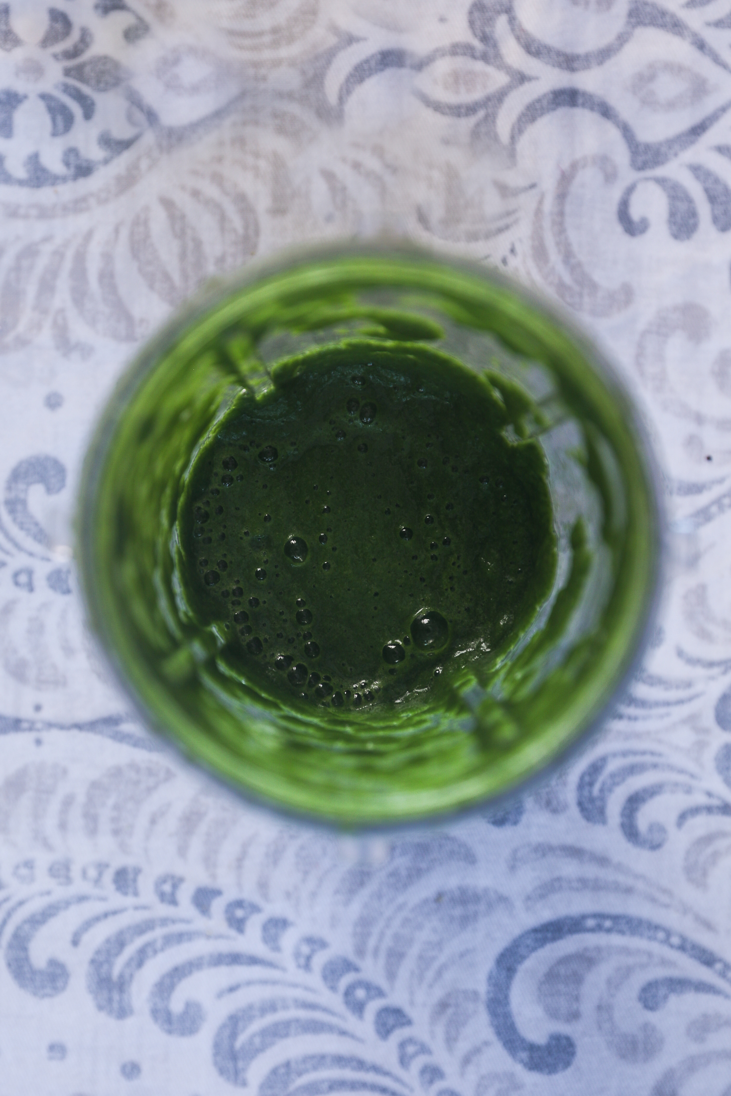 Top view image of a blender cup of green chutney with bubbles on top.