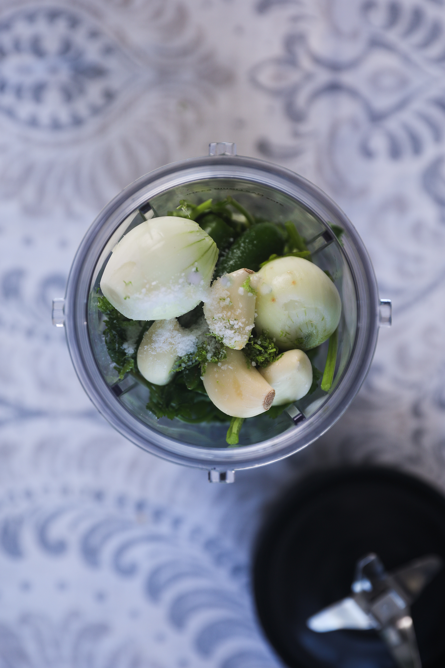 Top view image of a blender cup of greens, shallots, garlic and salt.