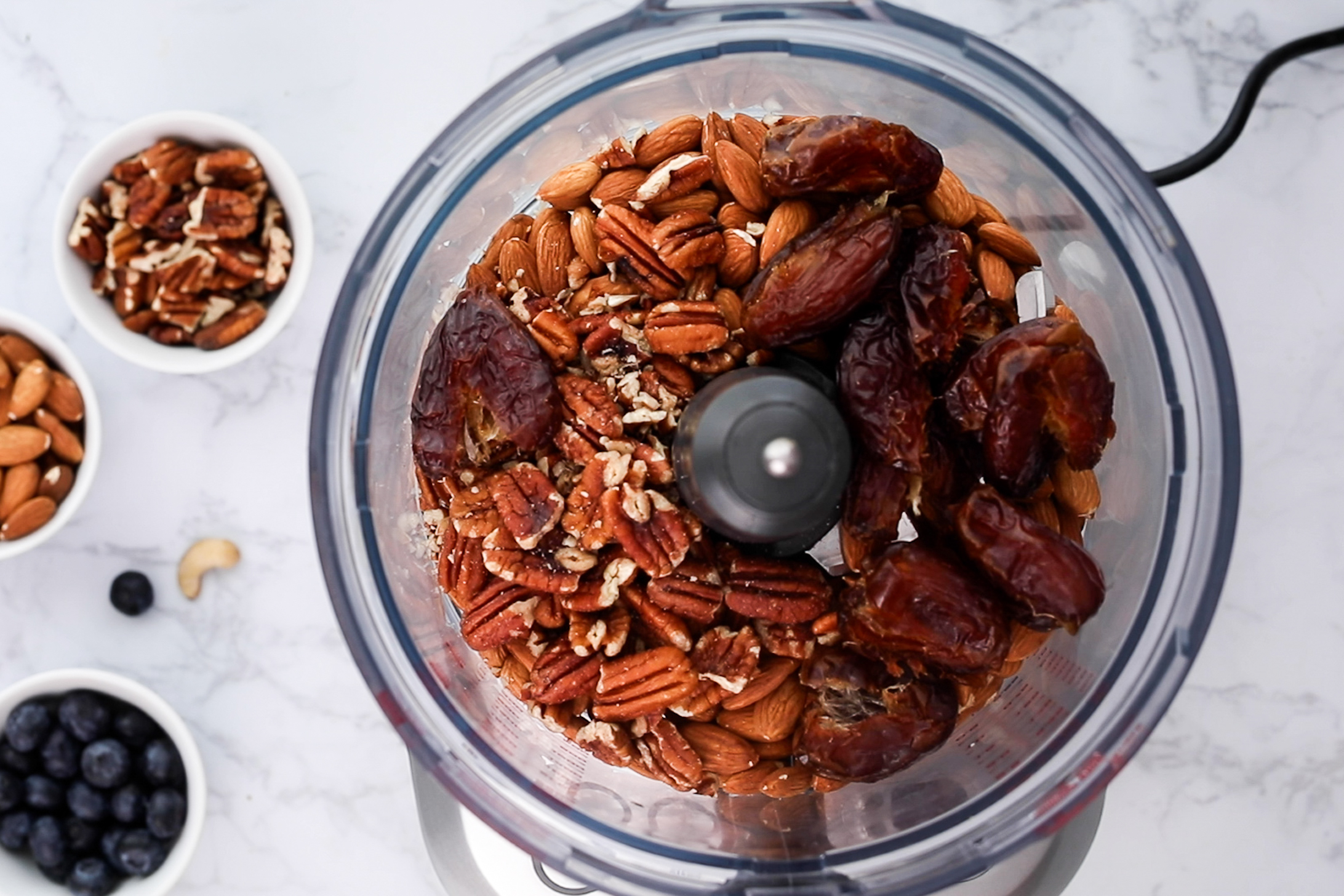 Top view of a food processor filled with dates, pecans and almonds.
