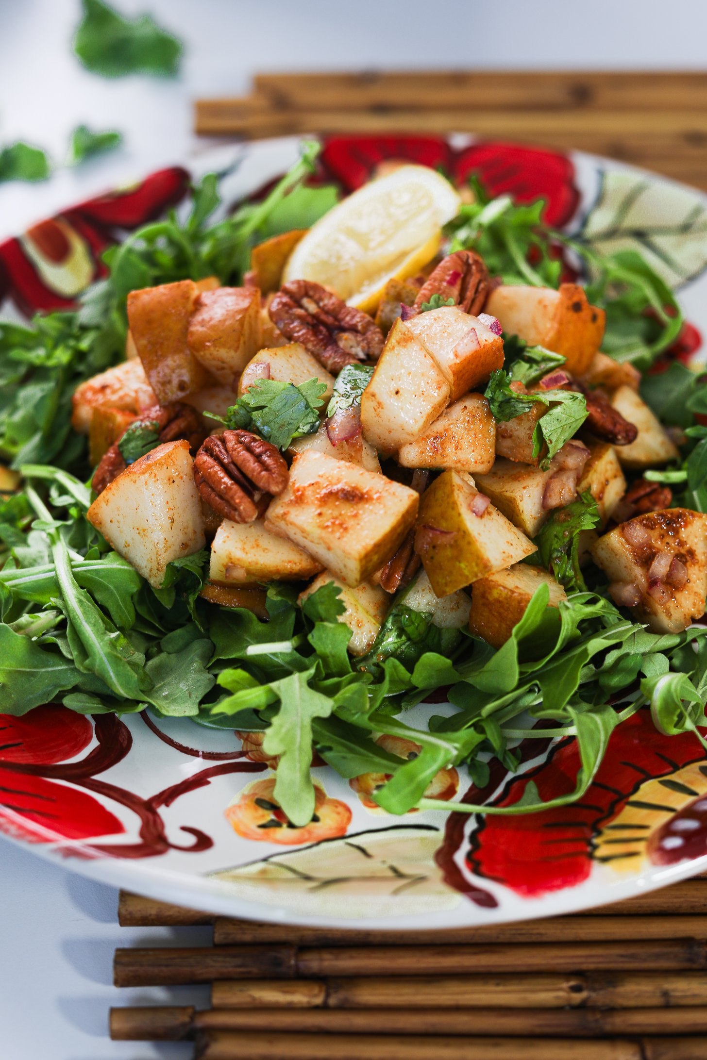 Close up image of Pecan and pear salad arranged atop a bed of rocket (arugula), garnished with cilantro and pecans, served on a floral-printed plate.