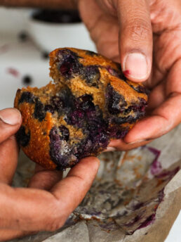 Perspective image of hands holding a blueberry muffin and opening it in half.