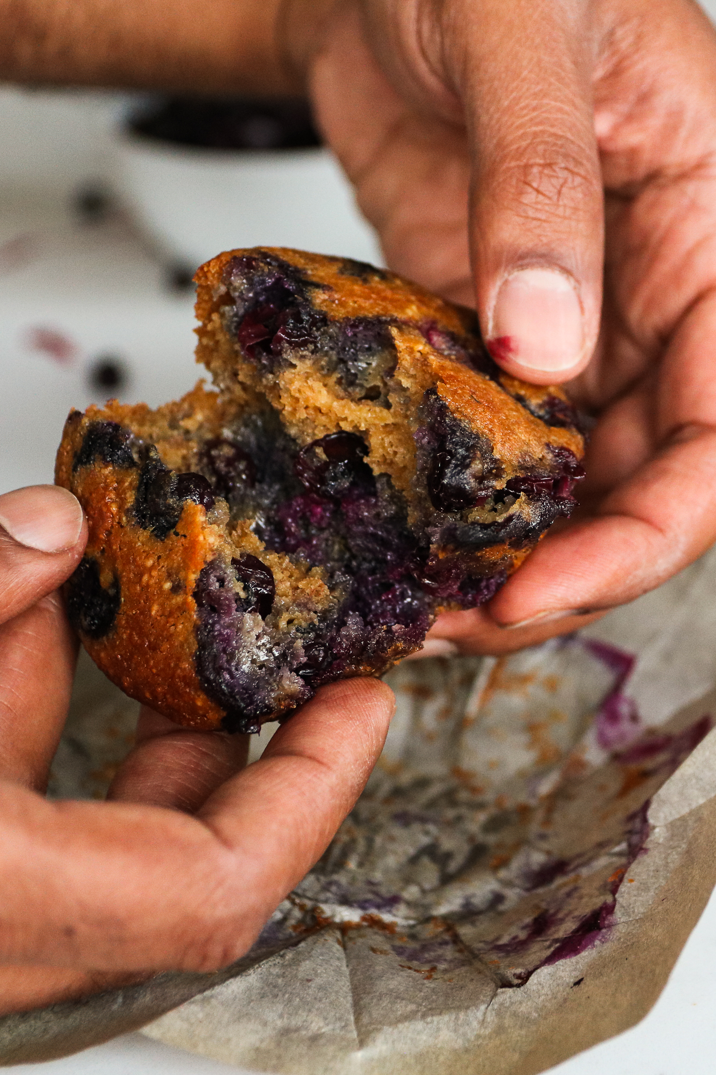 Perspective image of hands holding a blueberry muffin and opening it in half.