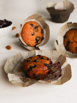 Image showing three blueberry muffins in liners laid at different angles, with berries in the background.