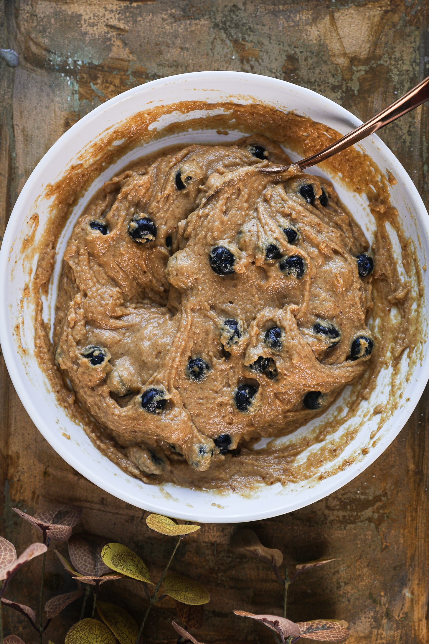 A bowl of brown muffin batter speckled with blueberries.