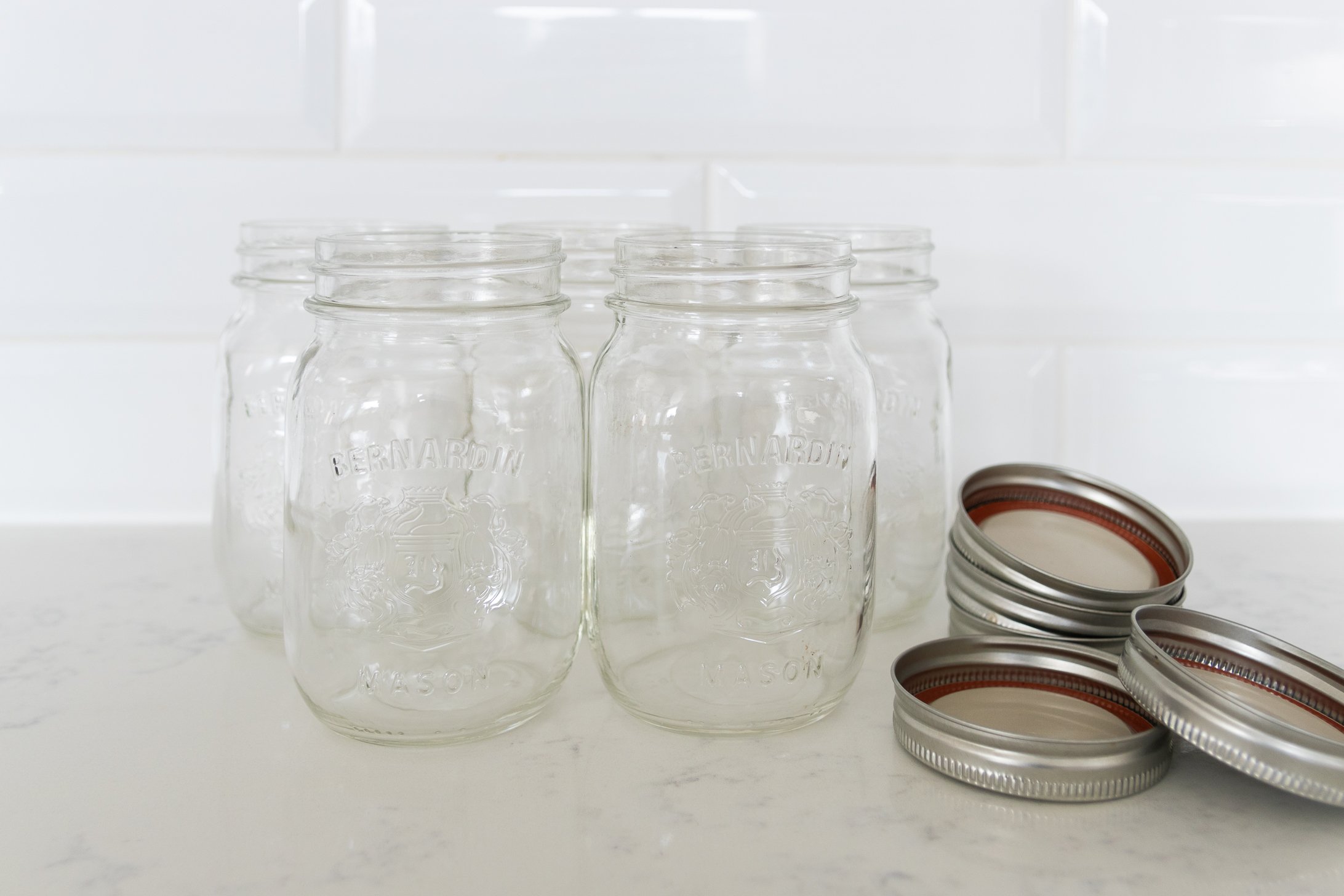 Five empty mason jars and lids leaning against a white background.