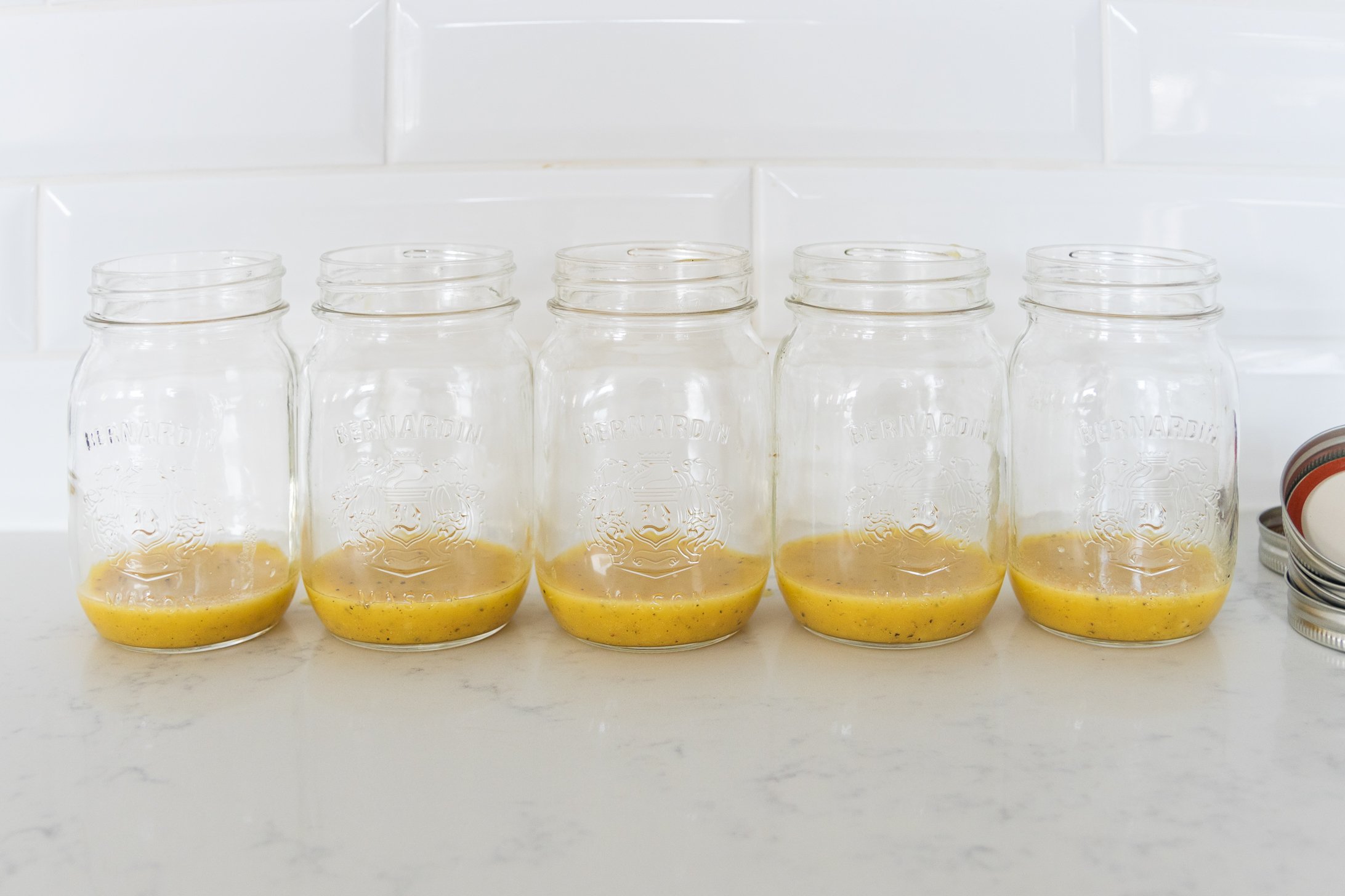 Five mason jars with dressing leaning against a white background.