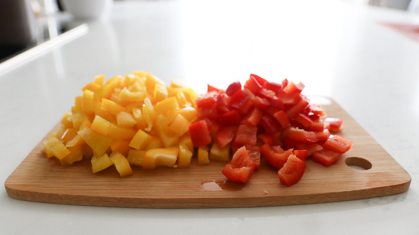 A chopping board with chopped red and yellow peppers.
