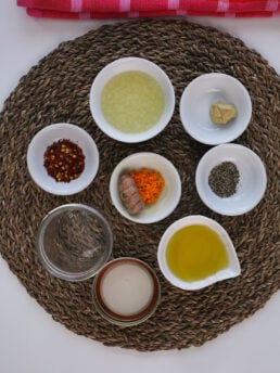 A selection of food ingredients like grated fresh turmeric, lemon juice, oil, and spices on a straw place mat.