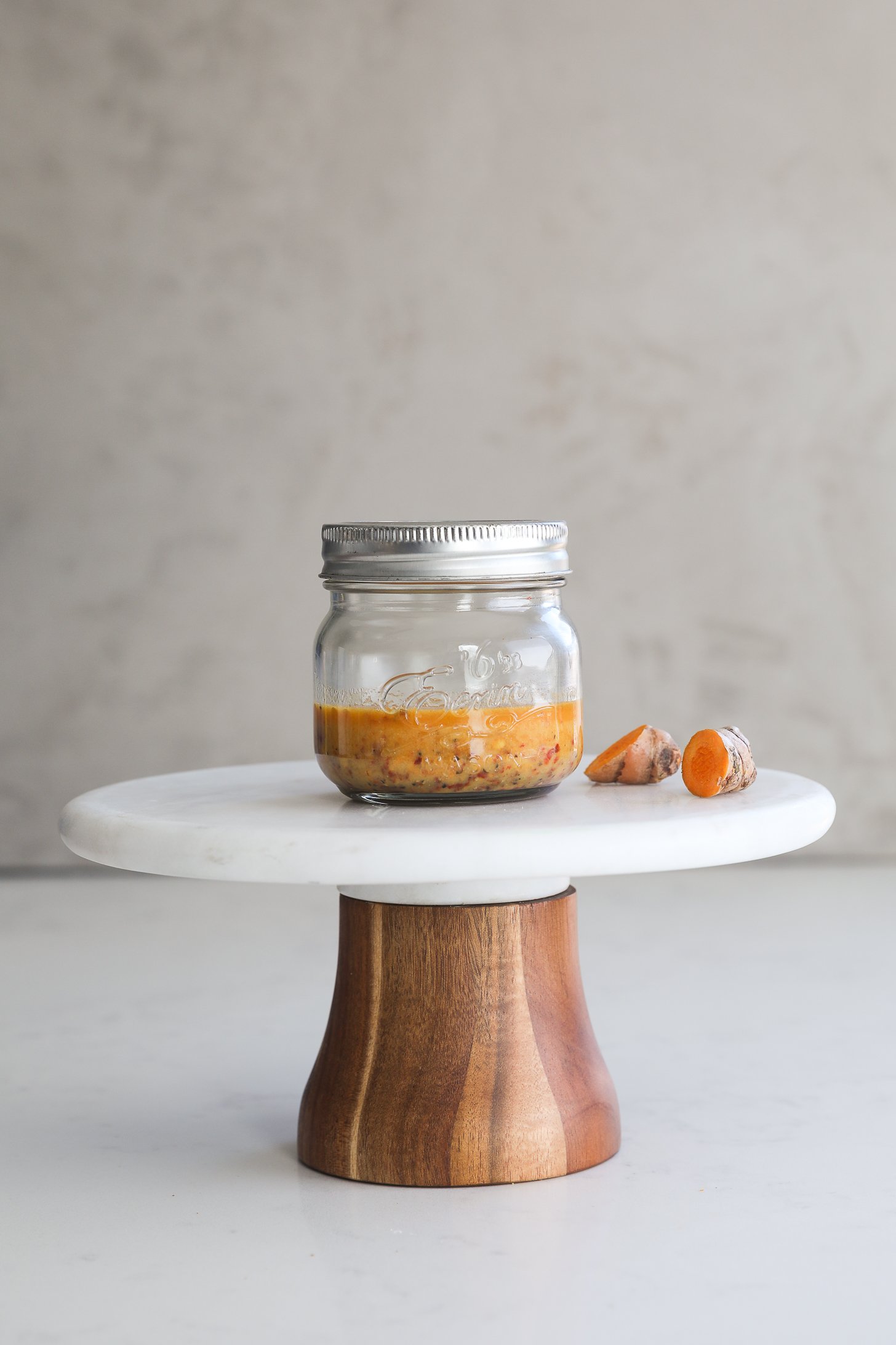 Small mason jar of orange-colored dressing placed on a white stand.