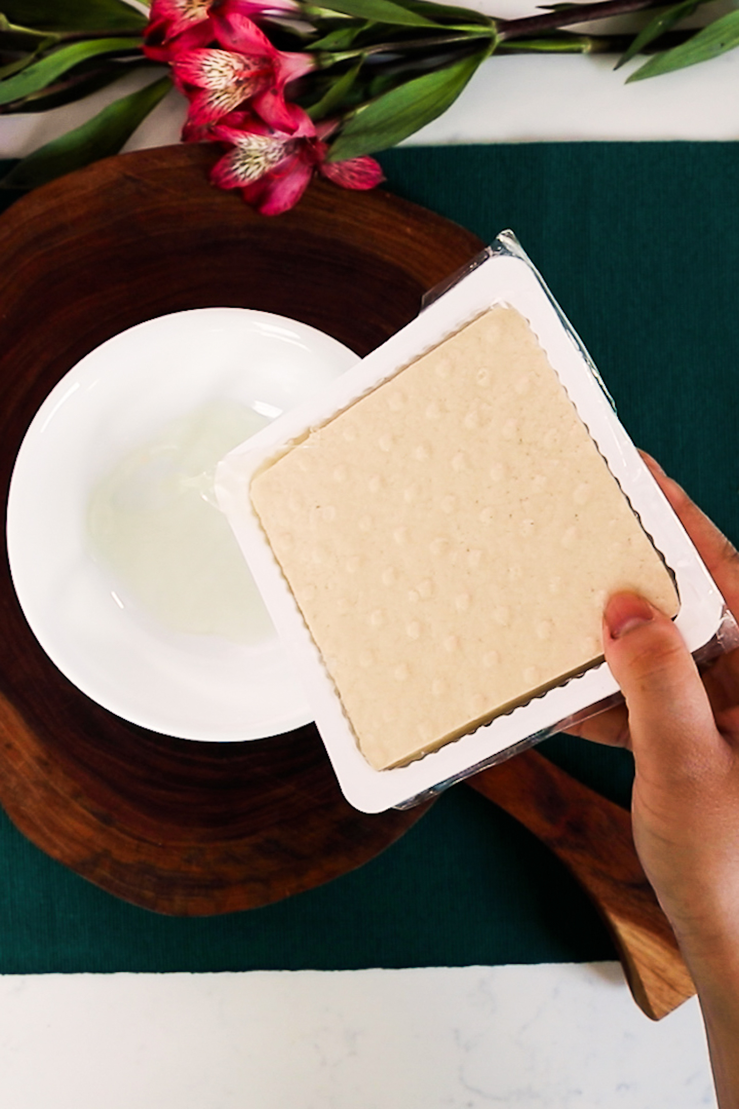 Hand holding a container with tofu and draining the liquid in a bowl.