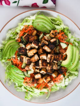 Top-down view of a generous salad plate featuring avocado slices, lettuce, carrot, cucumber, and topped with a heap of tofu cubes.