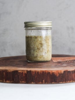 Perspective image of a mason jar with lemon oil dressing containing floating dried herbs.