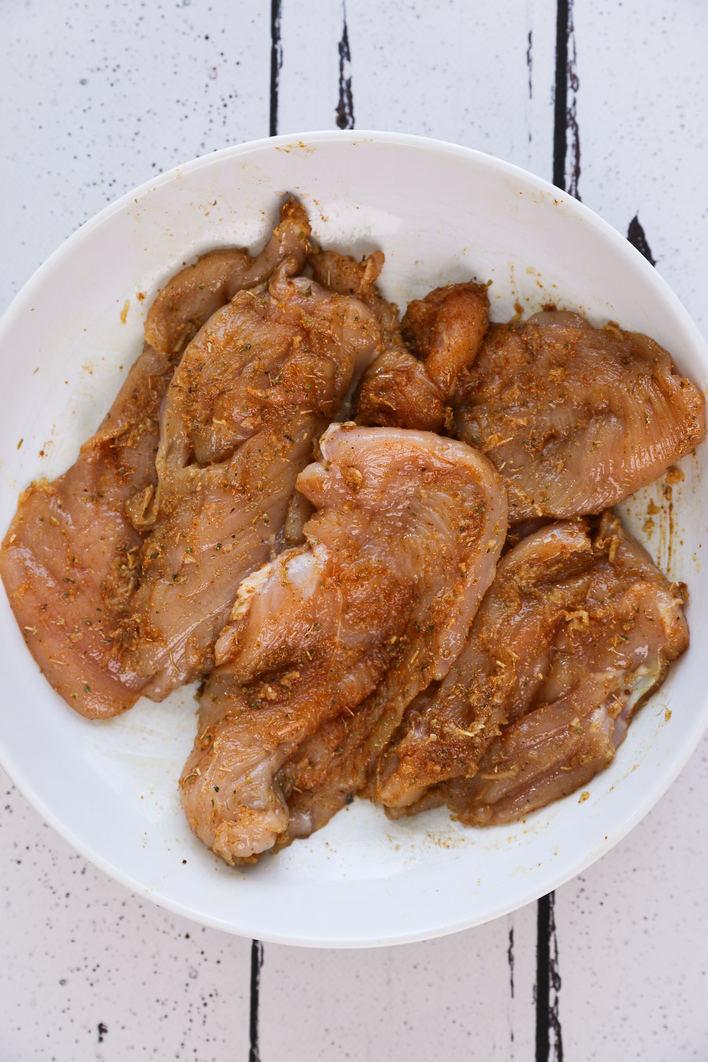 Spice-marinated slices of chicken in a bowl.