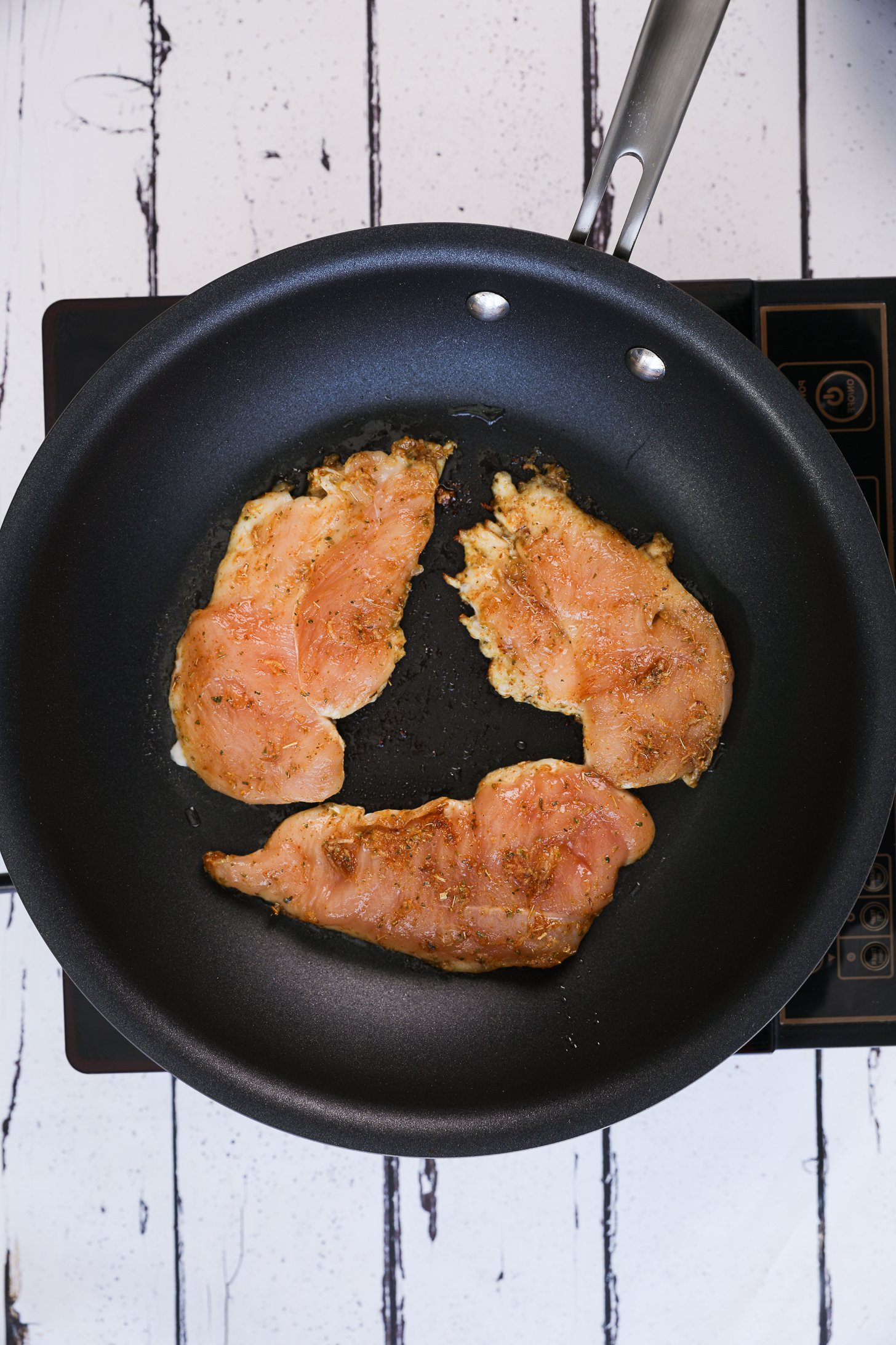 Spice-coated chicken slices frying in a pan on a mobile cooktop.