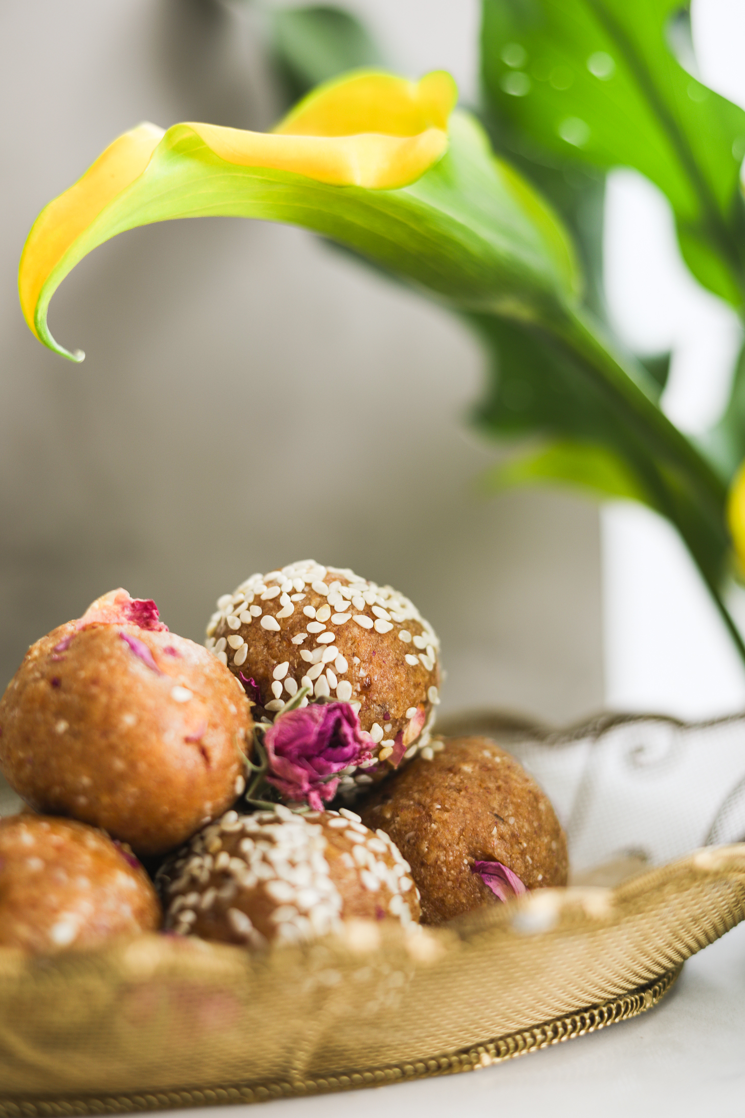 Close-up of brown energy balls, some coated with sesame seeds, with lilies nearby.
