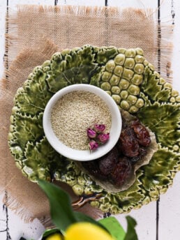 Green ceramic plate with a bowl of sesame seeds and dates on parchment paper.