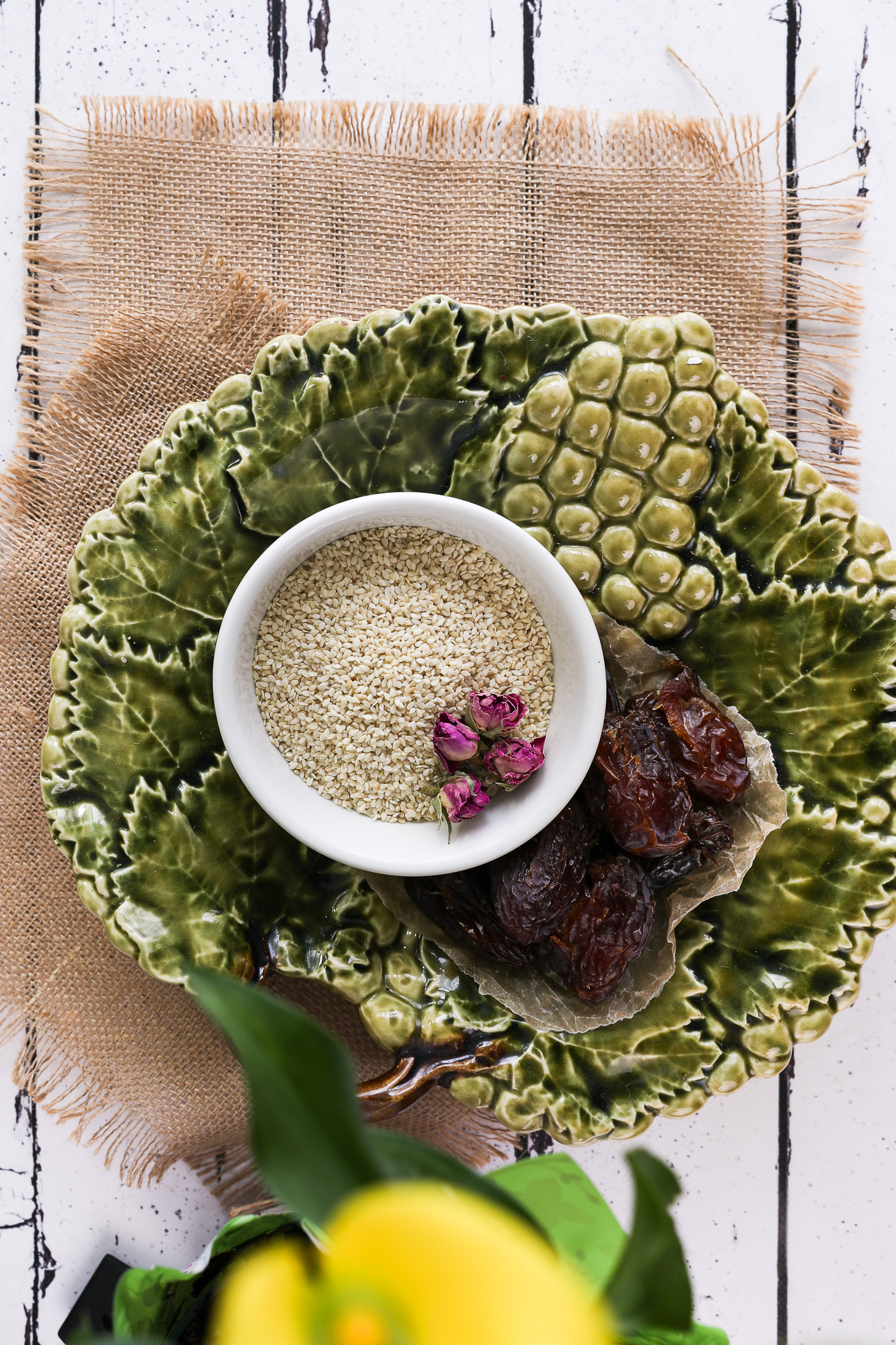 Green ceramic plate with a bowl of sesame seeds and dates on parchment paper.