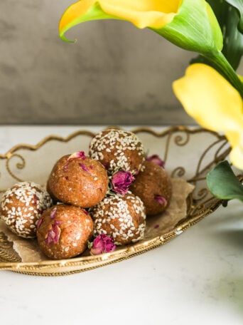 Perspective view of energy bliss balls, half coated in sesame seeds, with lilies in the foreground.