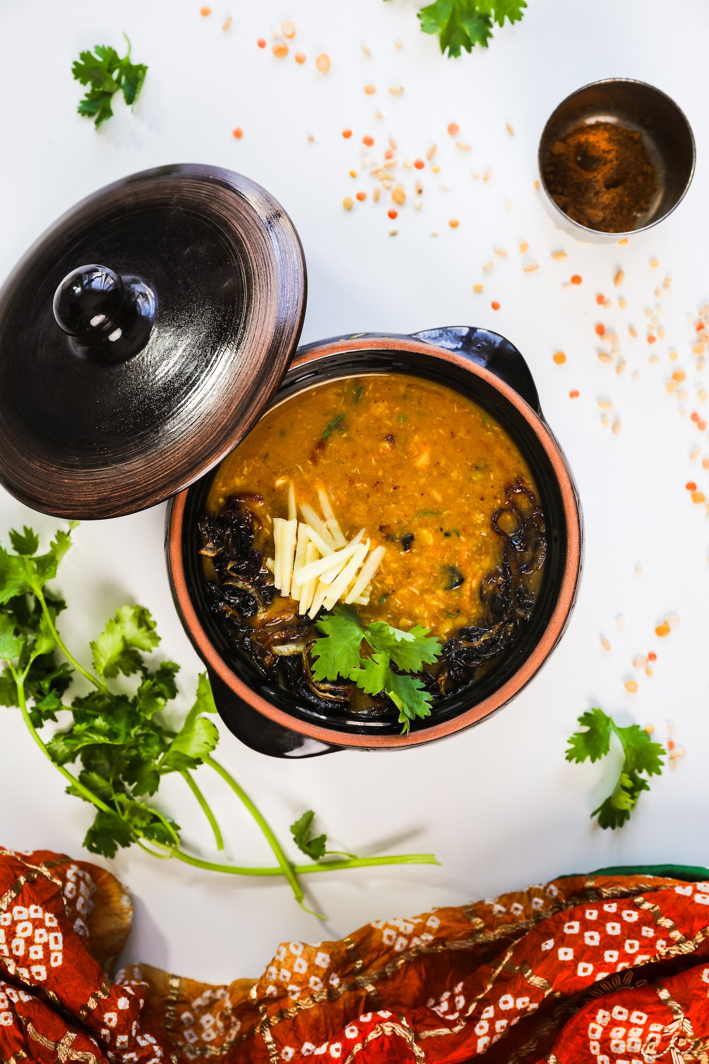 Birdseye image of a serving vessel with haleem, topped with fried onions, ginger strips, and cilantro leaves.