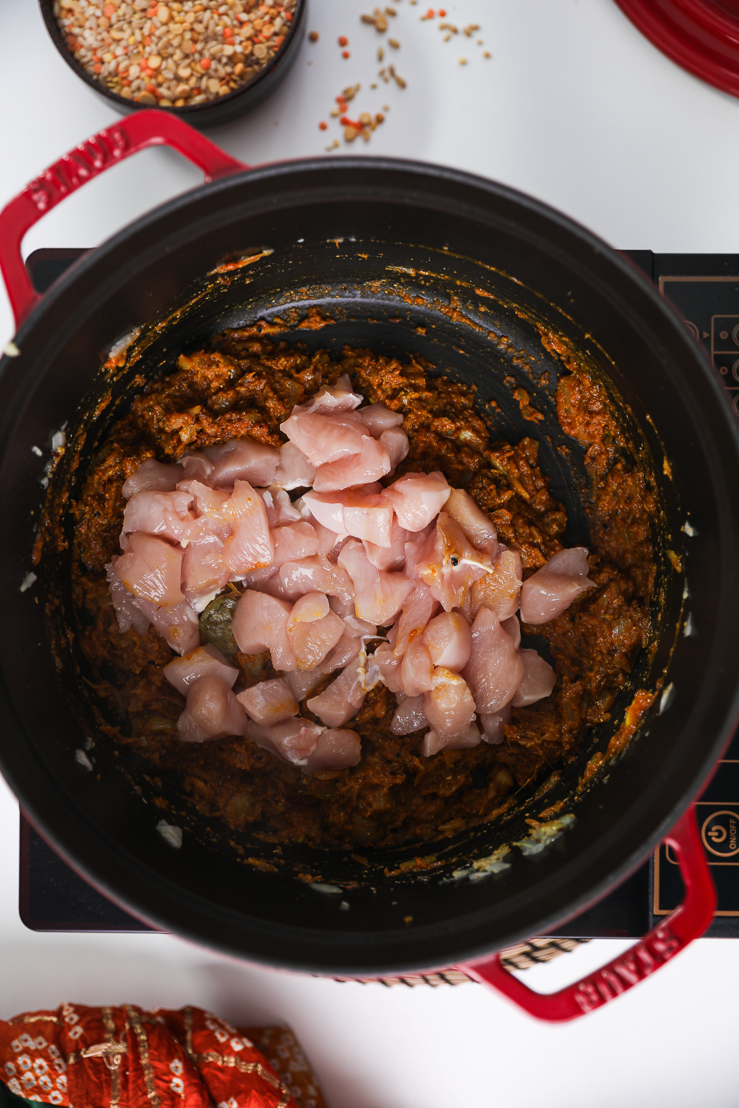Spiced tomato-onion mixture topped with chunks of chicken breast in a cook pot.