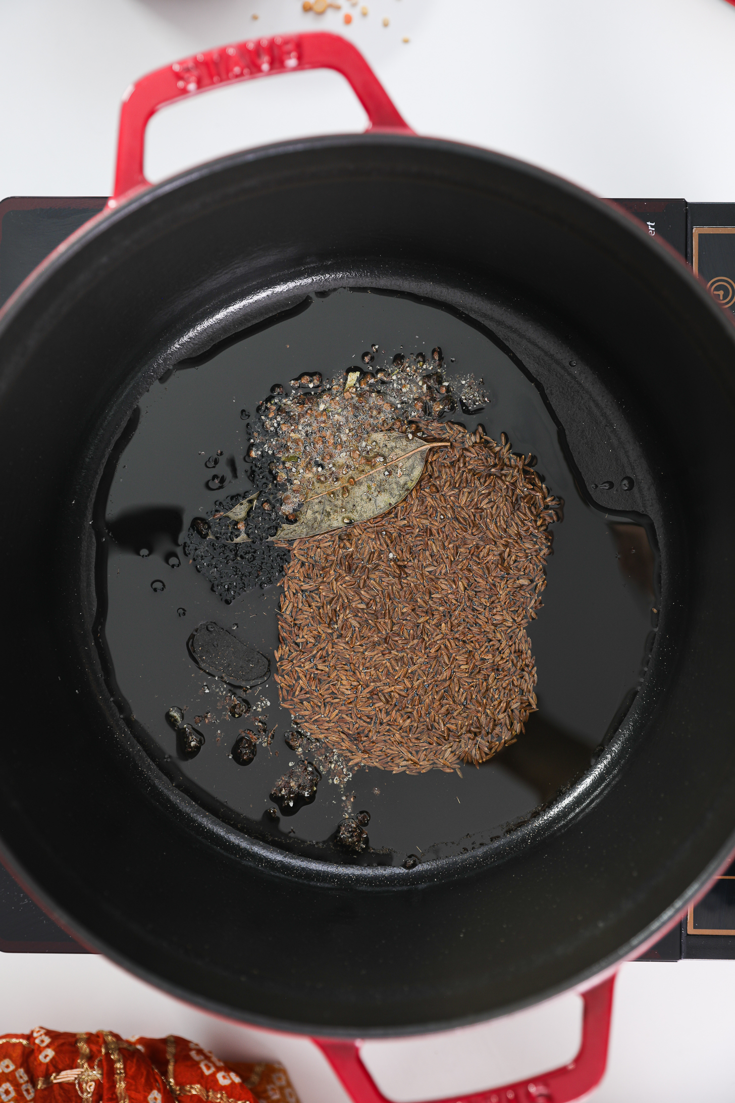 Cumin seeds, bay leaf, and other seeds tempering in oil in a cook pot.