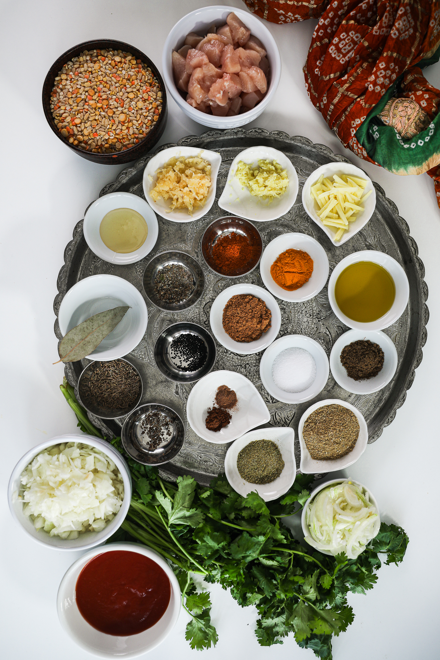 Indian spices on a round silver tray with bowls of chicken, lentils, onion, and tomato nearby.