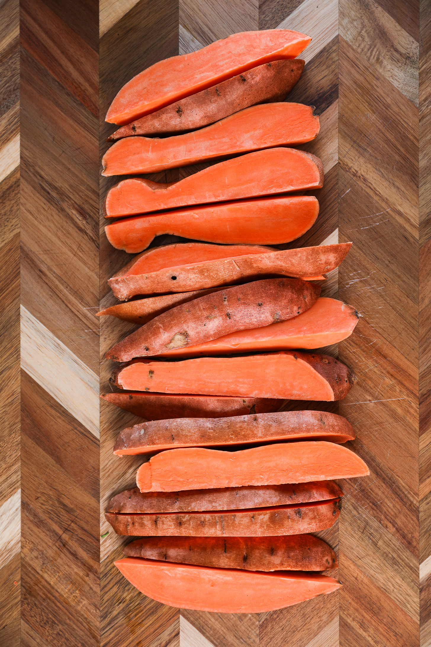 Raw sweet potato wedges neatly arranged on a wooden board.