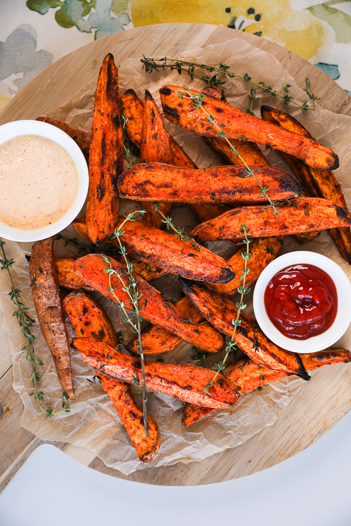 An overhead photo showcasing a stack of sweet potato wedges adorned with thyme sprigs, accompanied by two sauces nearby.