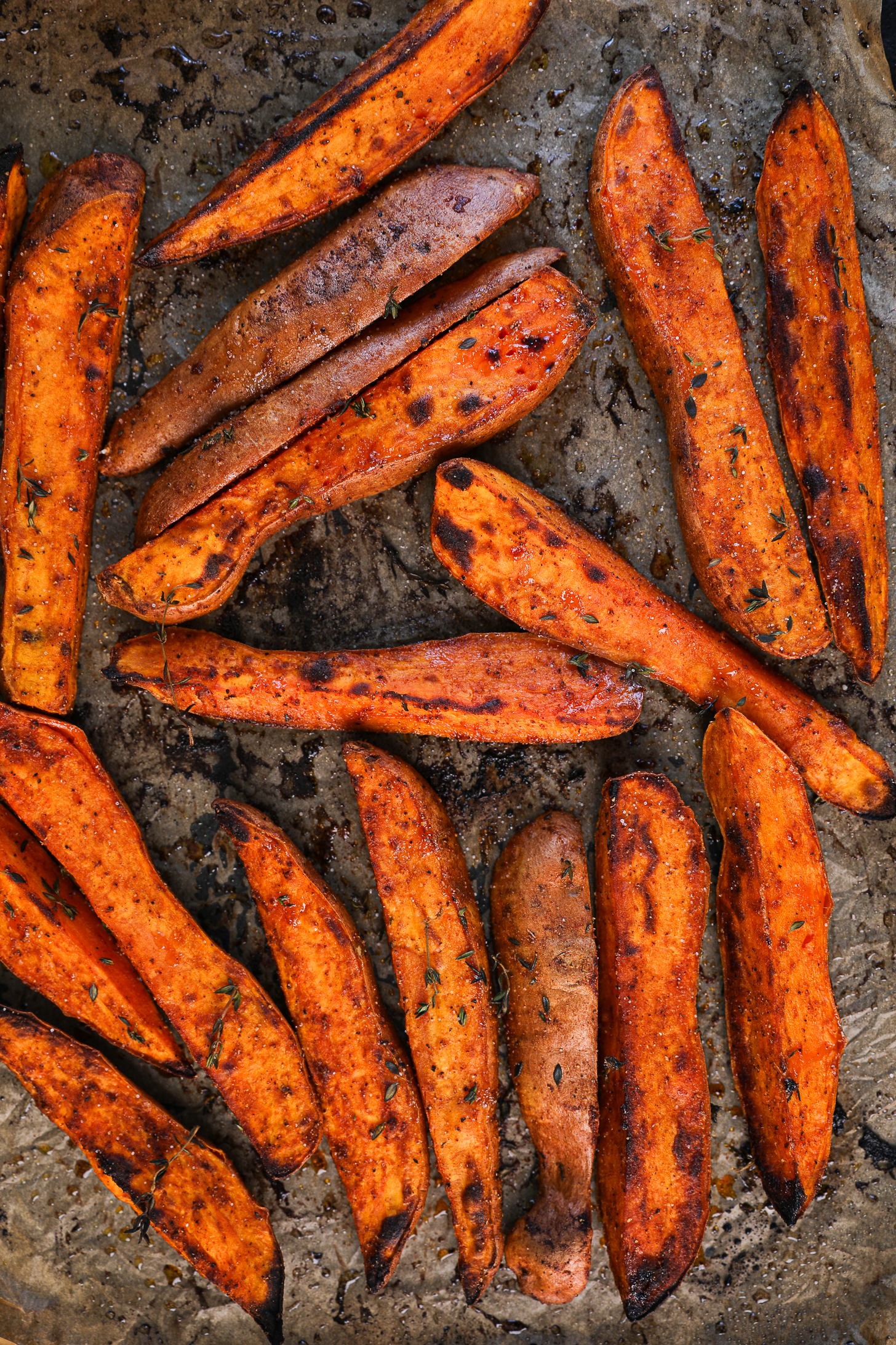 Charred roasted sweet potato wedges on a baking tray lined with parchment paper.