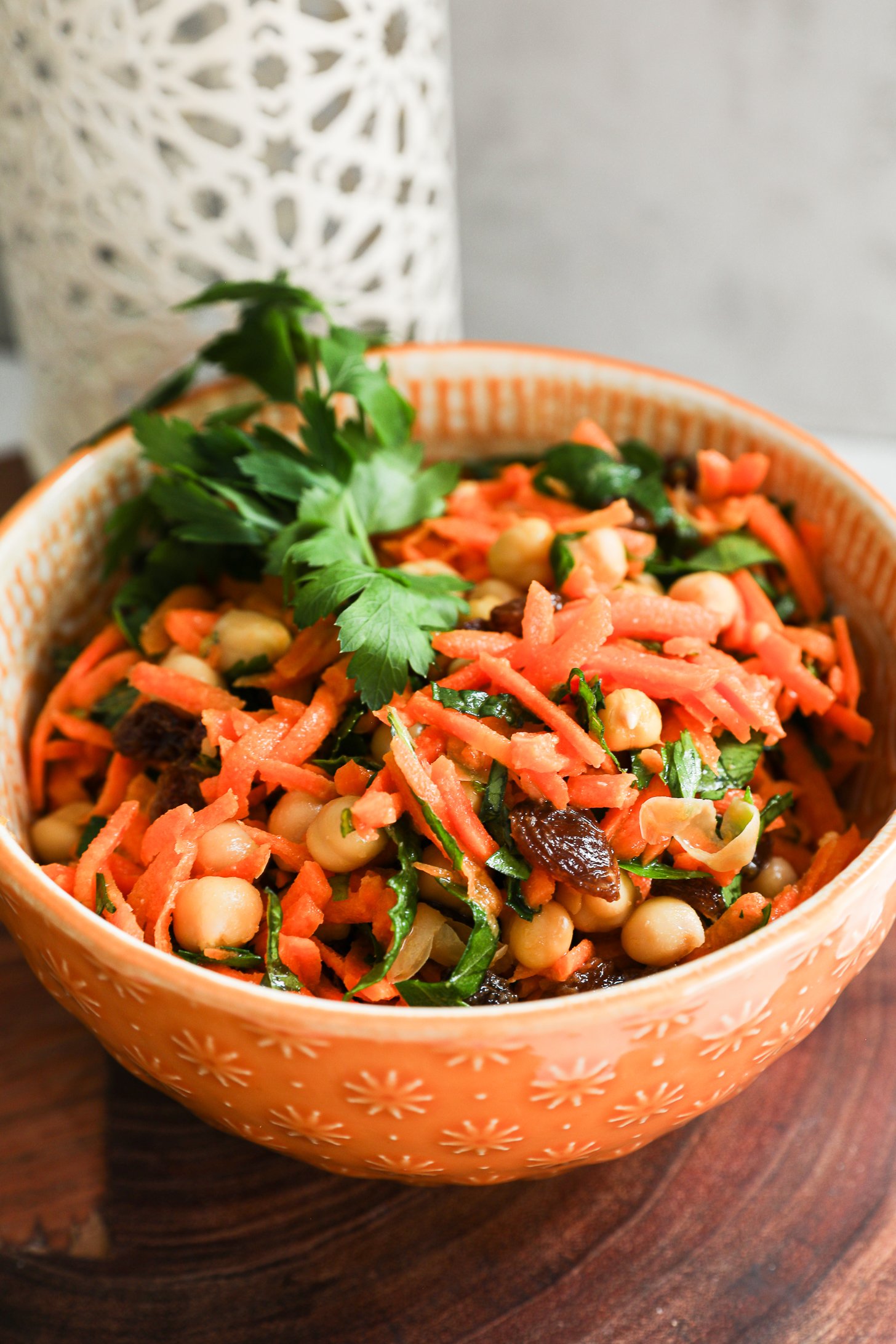Angled close-up of a bowl of grated carrot salad with chickpeas, raisins, and herbs.