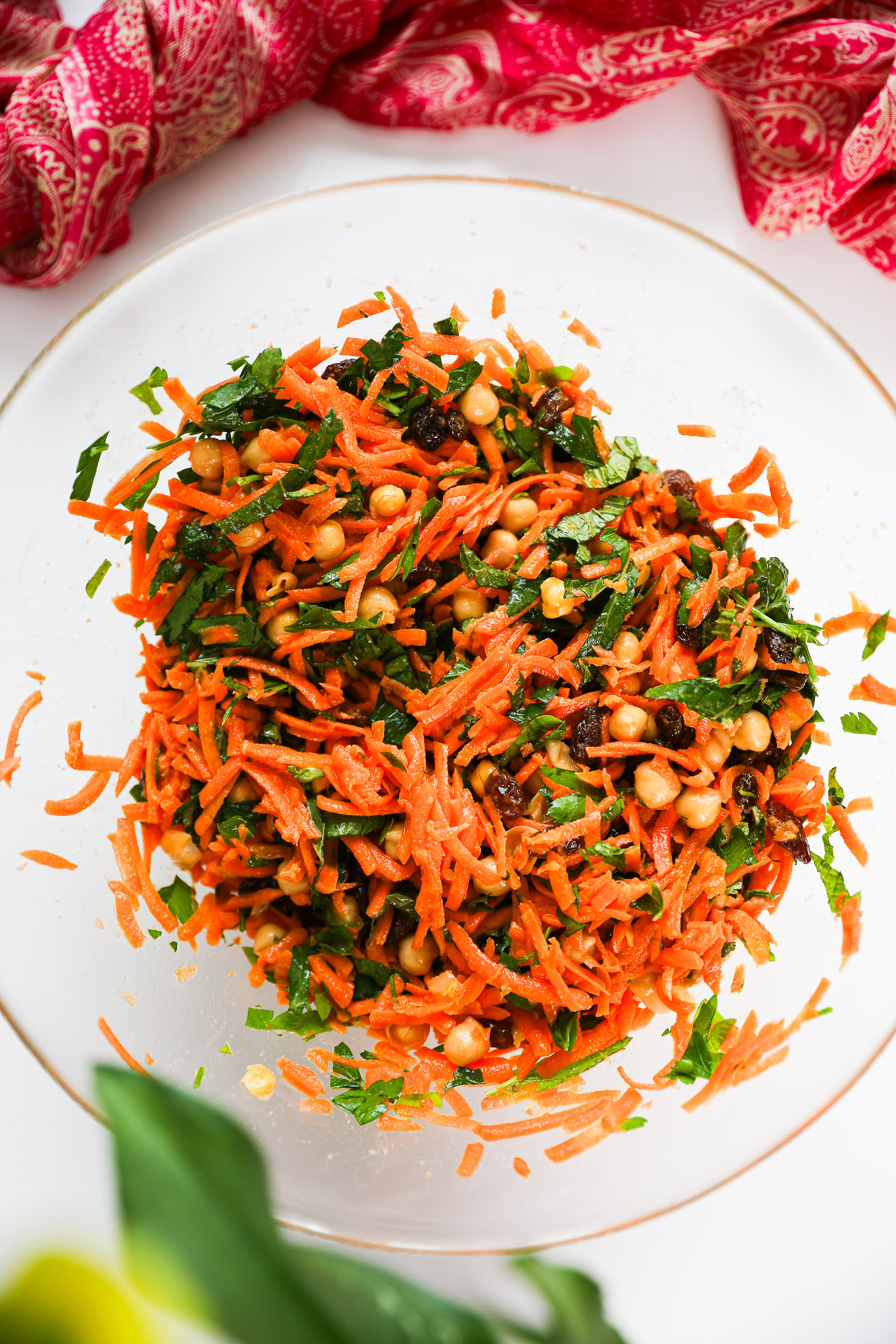 Overhead view of a salad bowl with grated carrots, chickpeas, raisins and herbs mixed together.